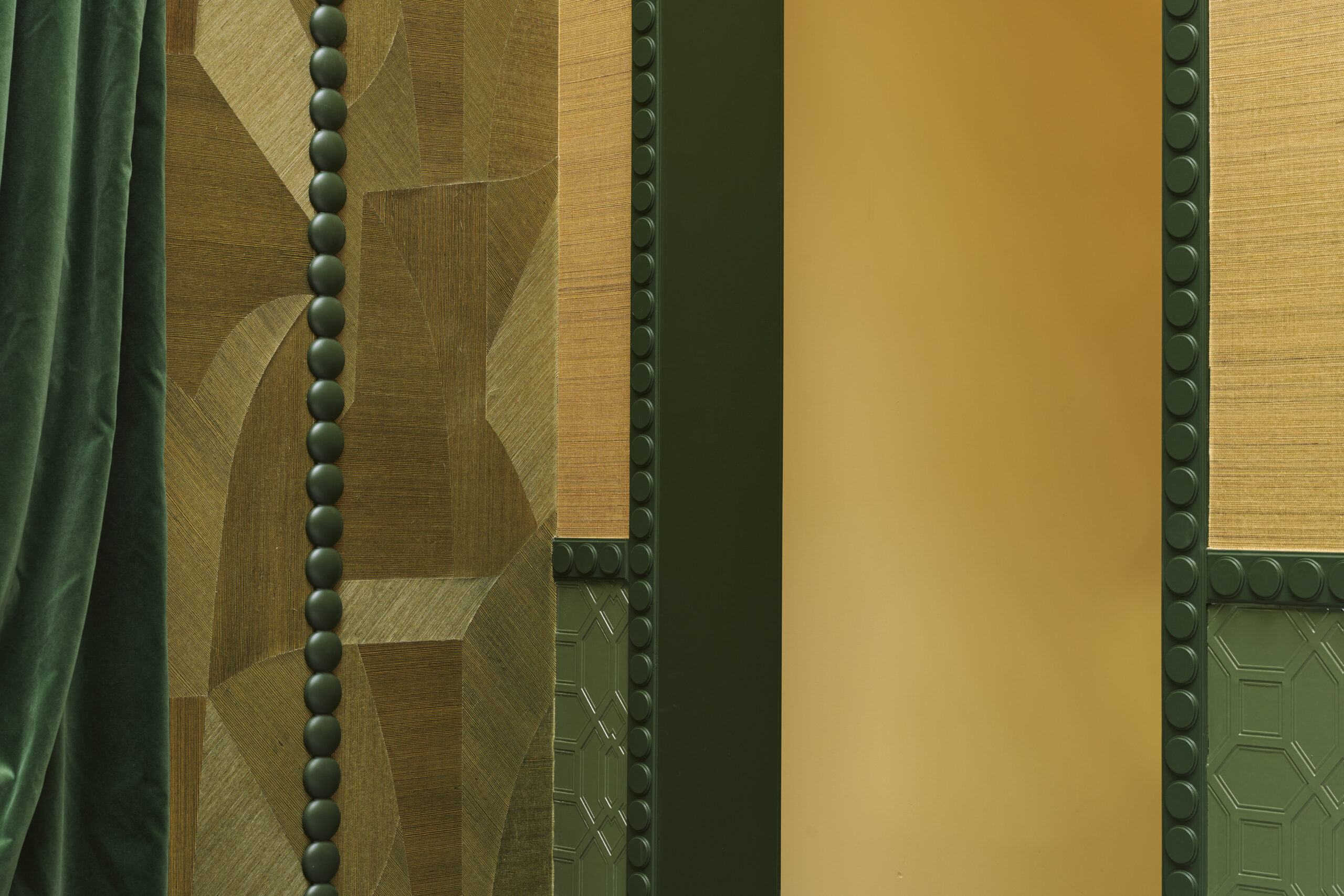 Decorative interior wall with a green velvet curtain, geometric wood panels, and olive-green and gold panels with studded edges.