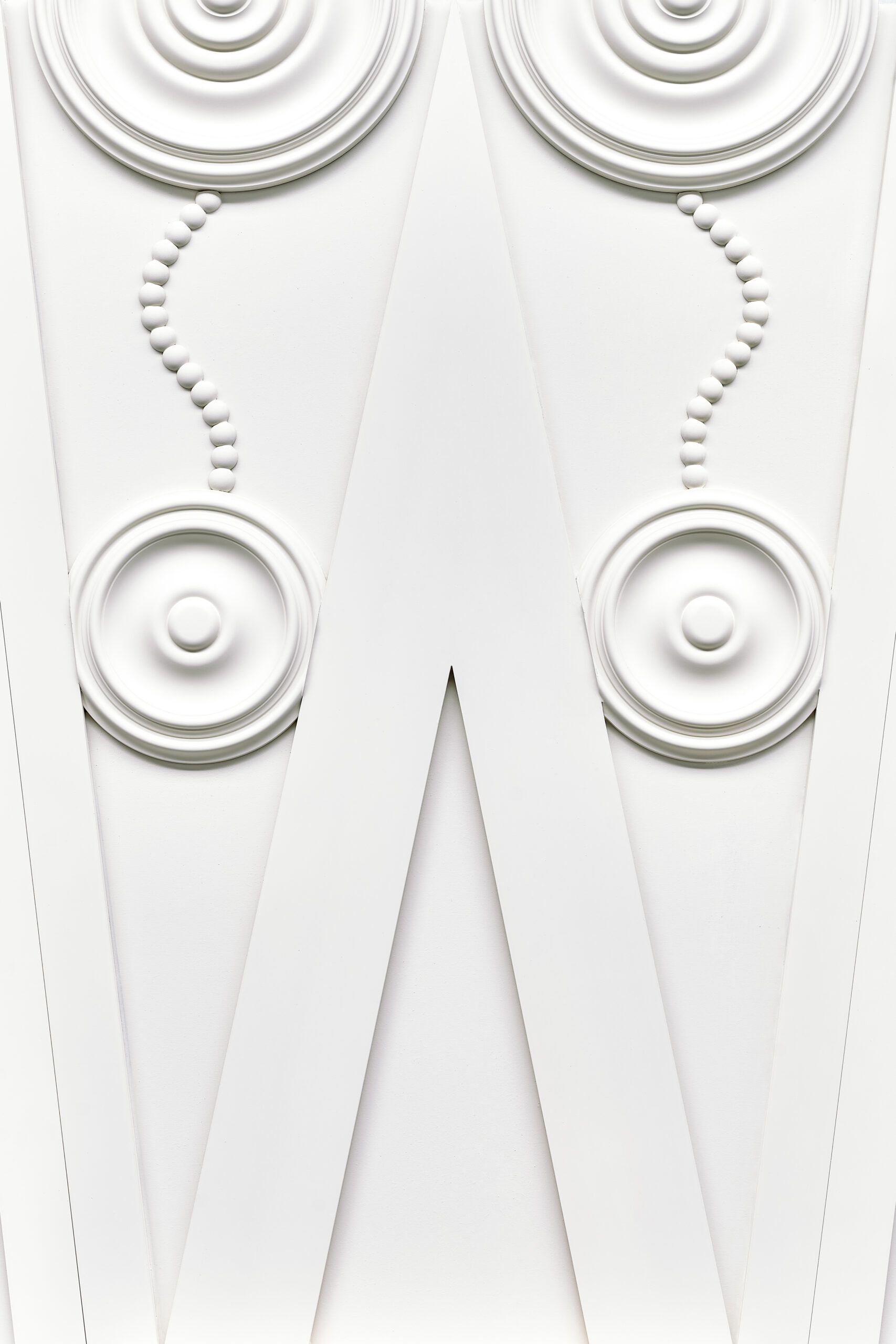 Abstract white sculpture with circular discs and bead strands forming a symmetrical V pattern in high contrast lighting.