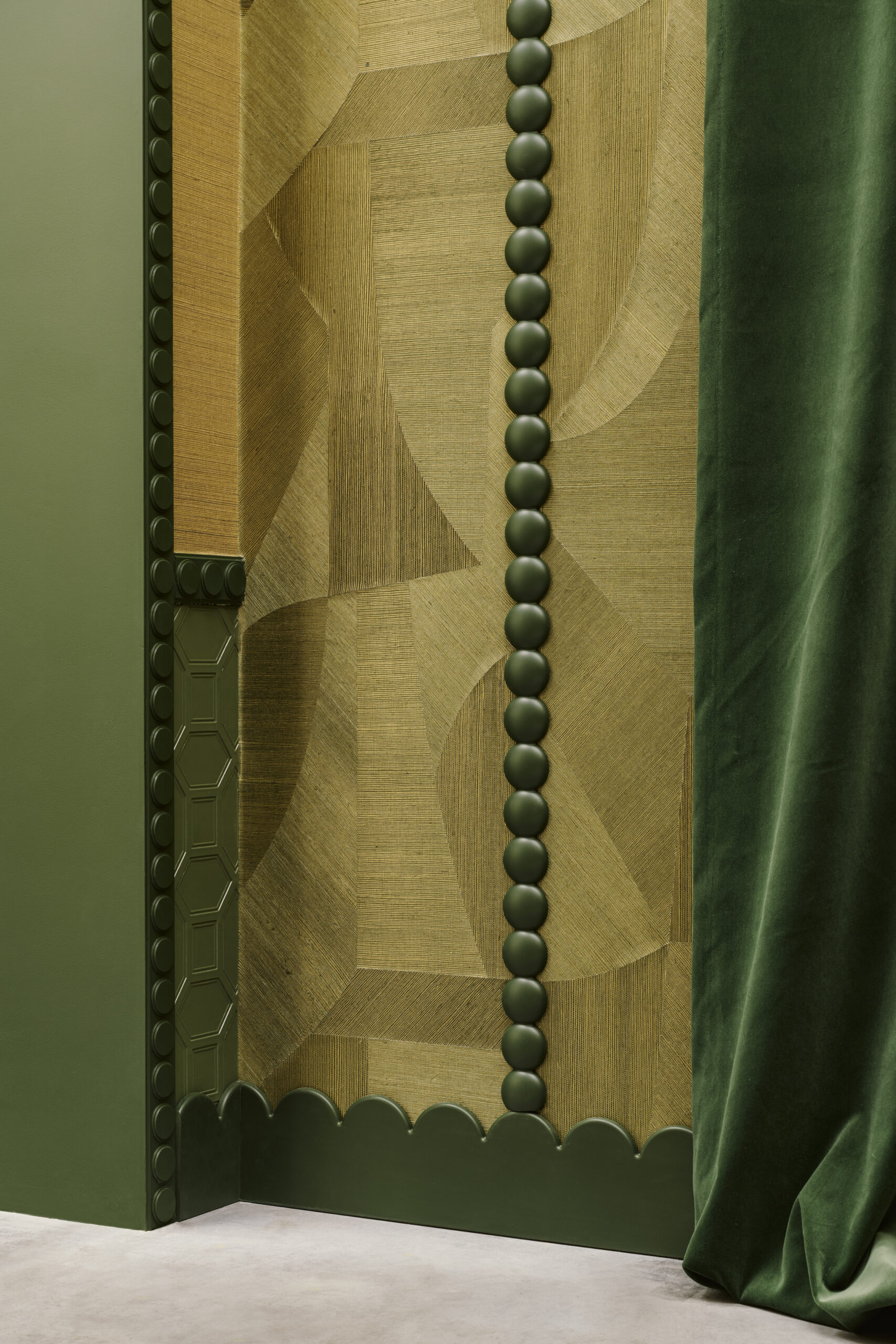 Green wall with a vertical string of dark green beads, against geometric tan wallpaper and a green velvet curtain behind.