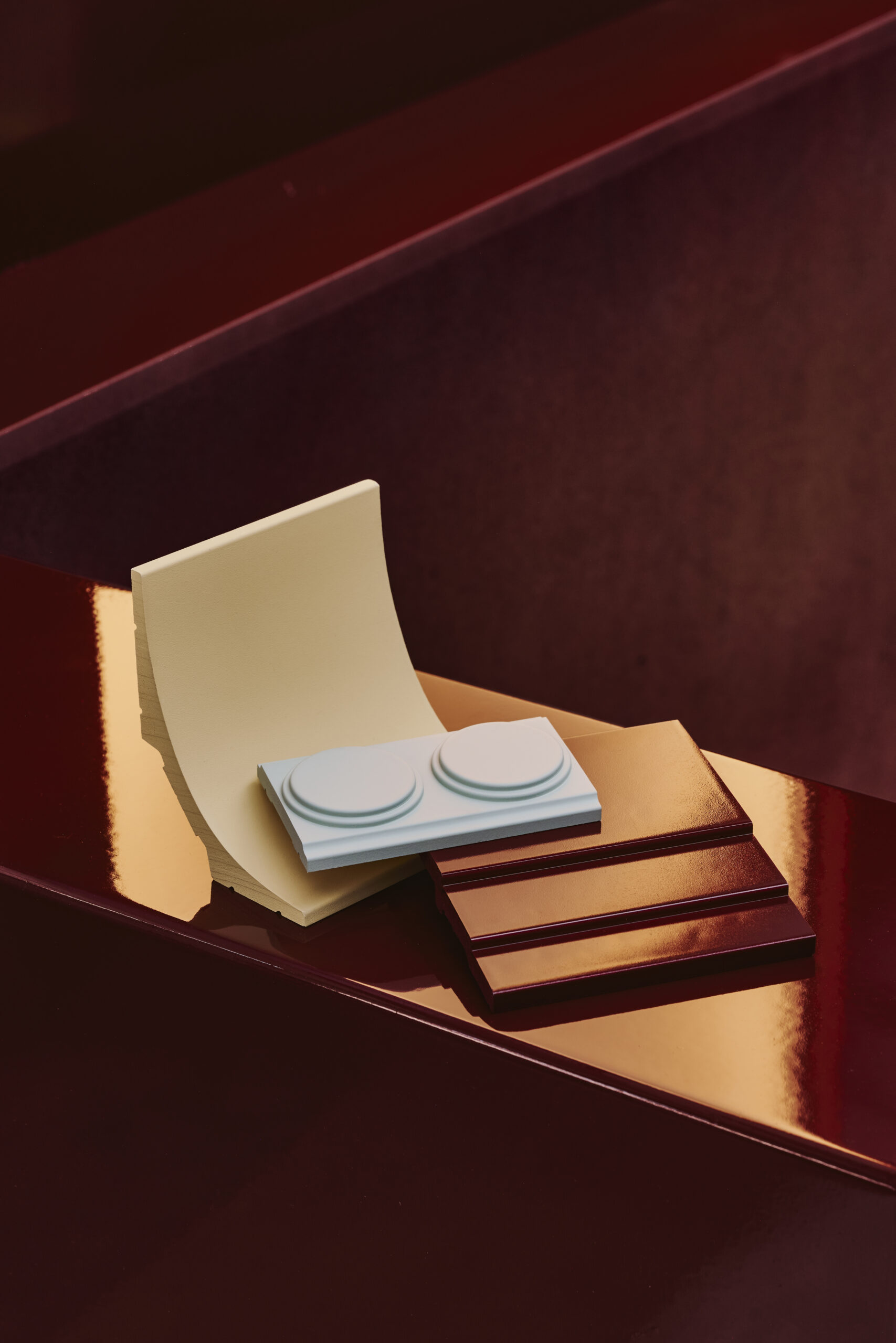Close-up of a pale yellow curved sheet and a light blue LEGO brick resting on a bar of chocolate on a glossy dark red surface.